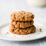 Baked almond butter cookies on a white plate with crumbs and a glass of almond milk.