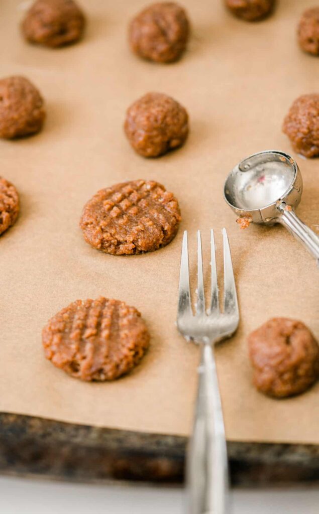 Almond butter dough on parchment paper on a tray with a fork and cookie scoop
