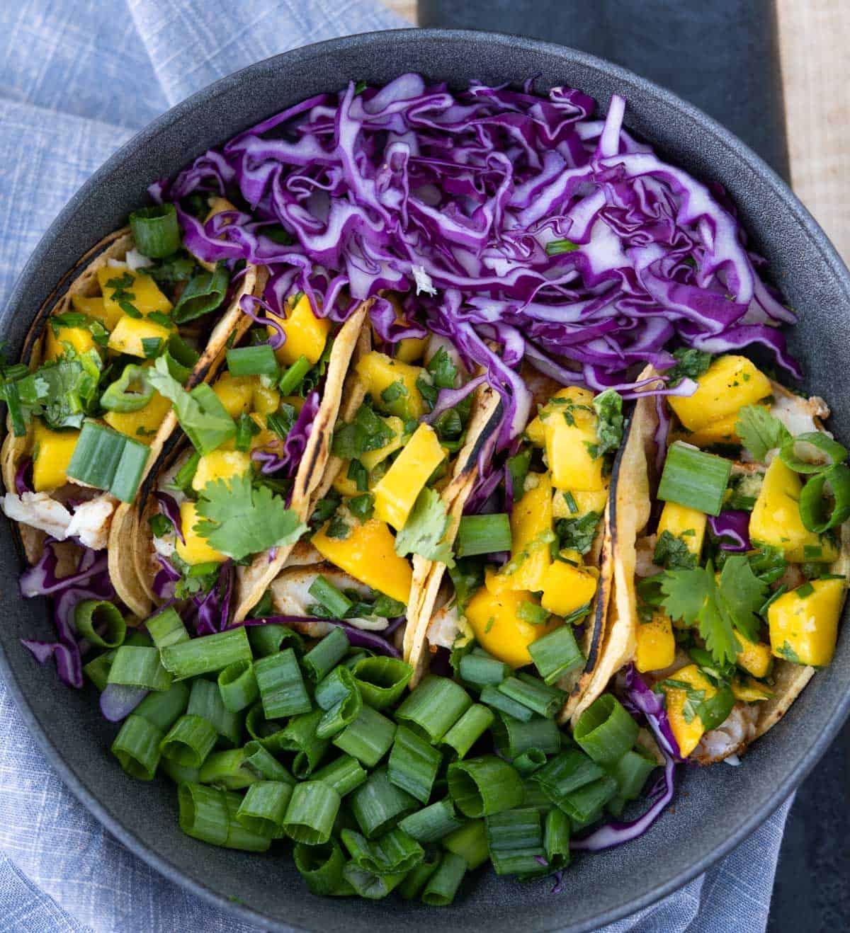 White fish taco with mango mint salsa on a dark plate with chopped red cabbage and scallions