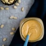 peanut butter in mason jar with spoon and scattered peanuts.