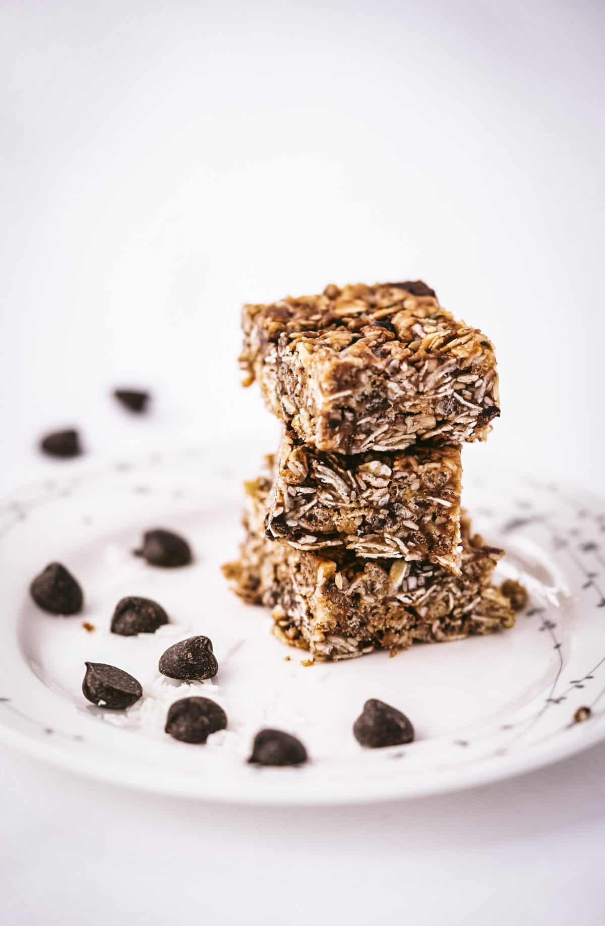 chewy chocolate chip granola bars stacked on a plate with a scattering of chocolate chips