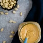 peanut butter in mason jar with spoon and scattered peanuts.