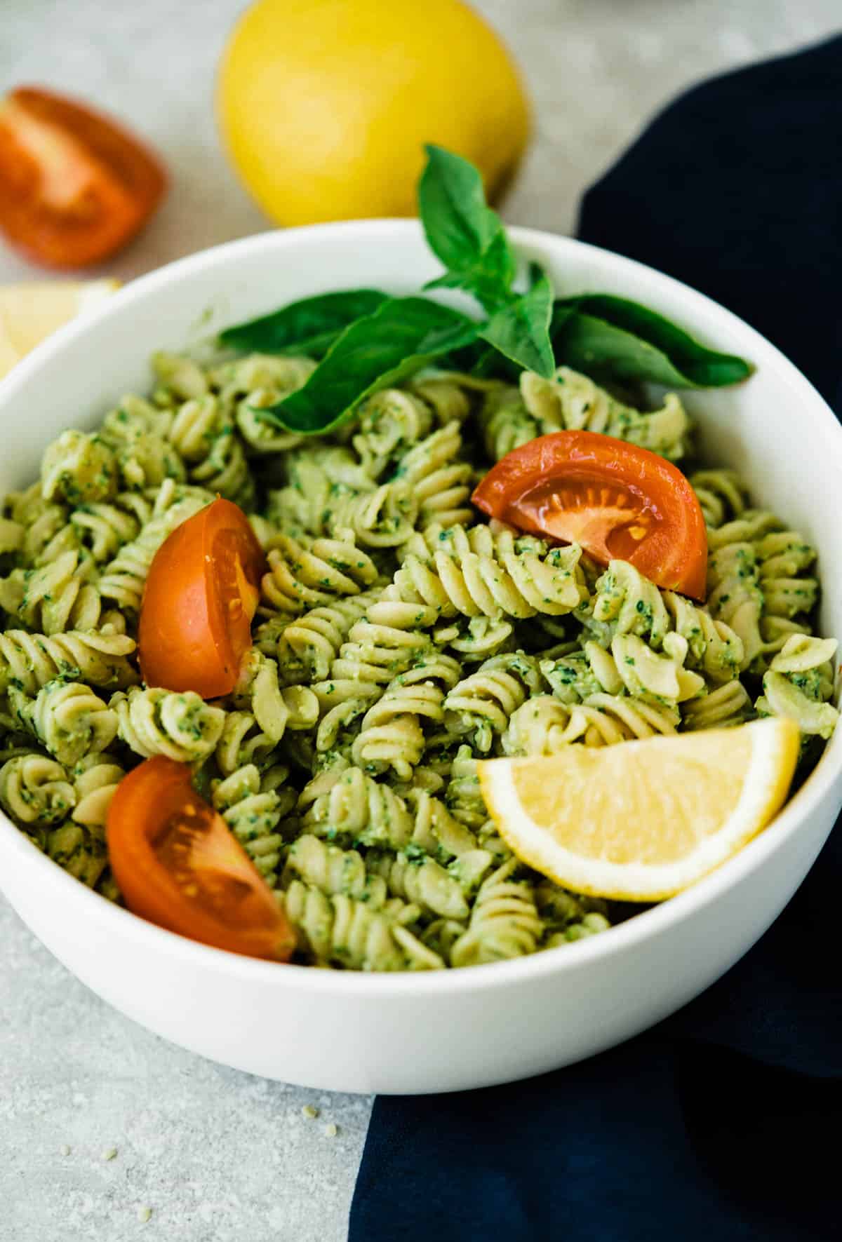 Creamy avocado pesto pasta in a dish with lemon and tomatoes