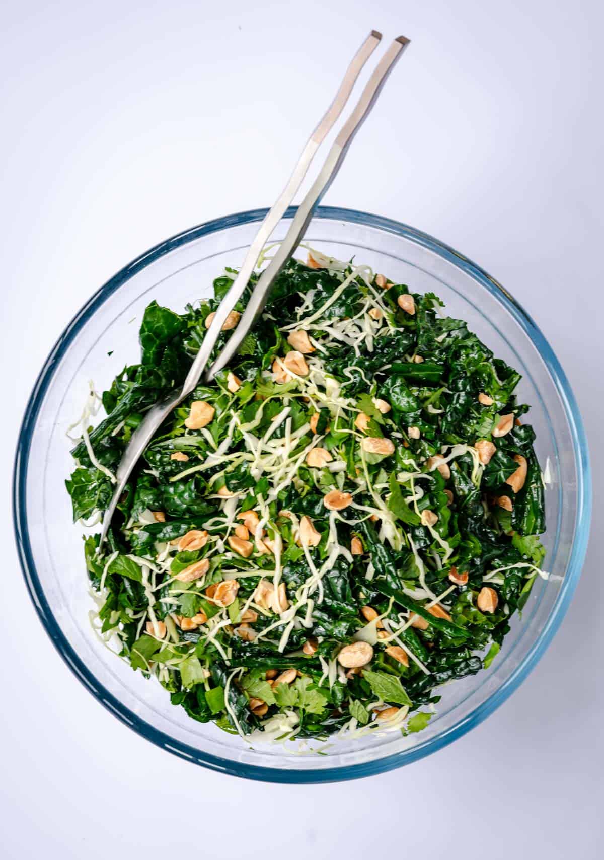 crunchy kale salad with spicy peanut vinaigrette in a bowl with tongs to serve