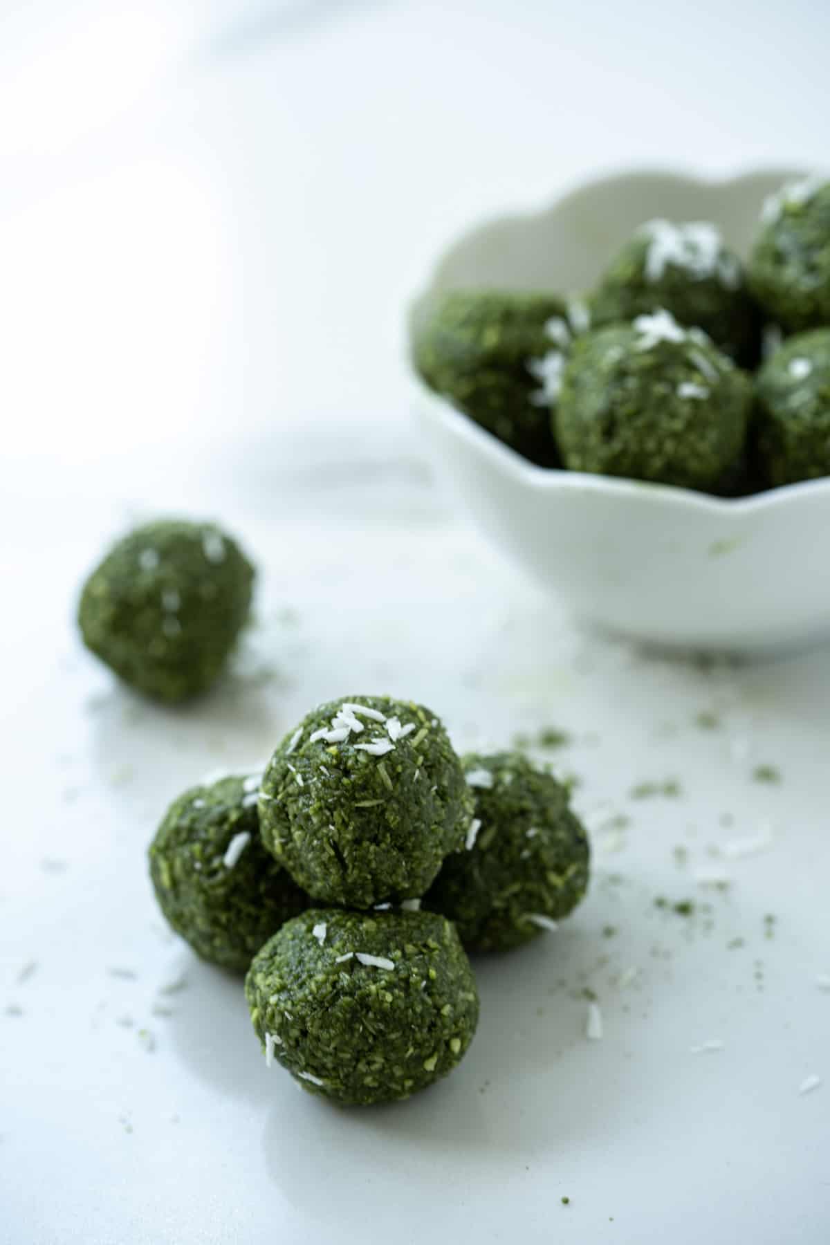 Matcha bliss balls piled on the counter with a full white bowl in the background