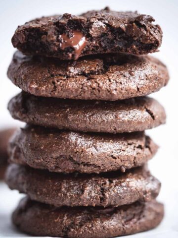 chocolate fudge tahini cookies stacked with a bite out of the top cookie