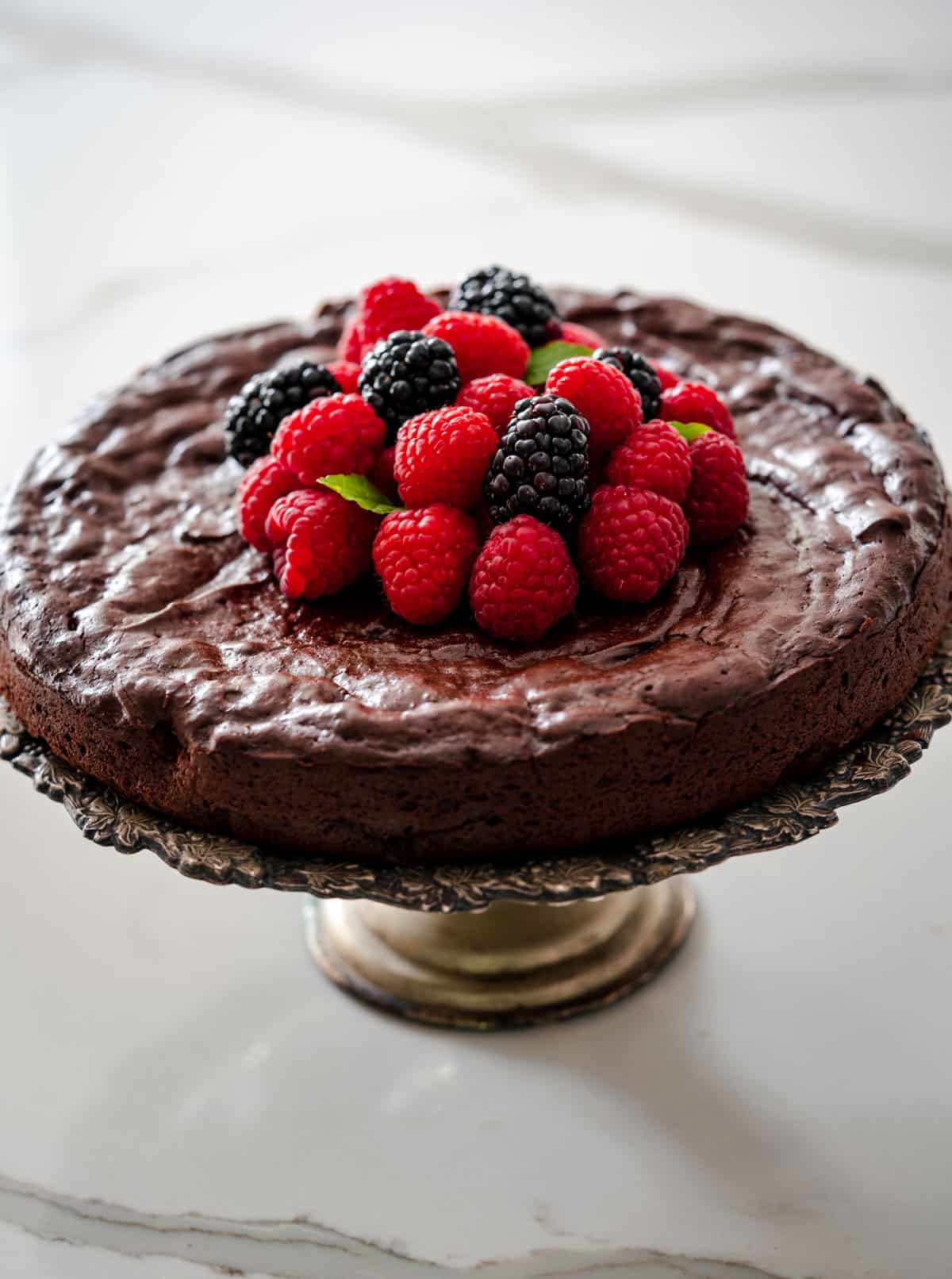 baked flourless chocolate cake on a silver cake stand with berries on top