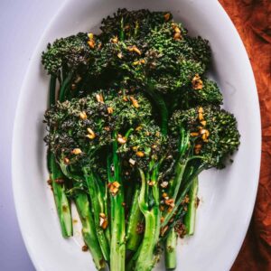 roasted broccolini on a white dish dressed with soy, garlic, ginger dressing