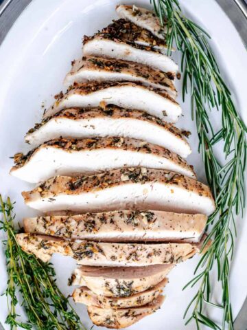 roasted turkey breast sliced on a serving platter with fresh rosemary and thyme.