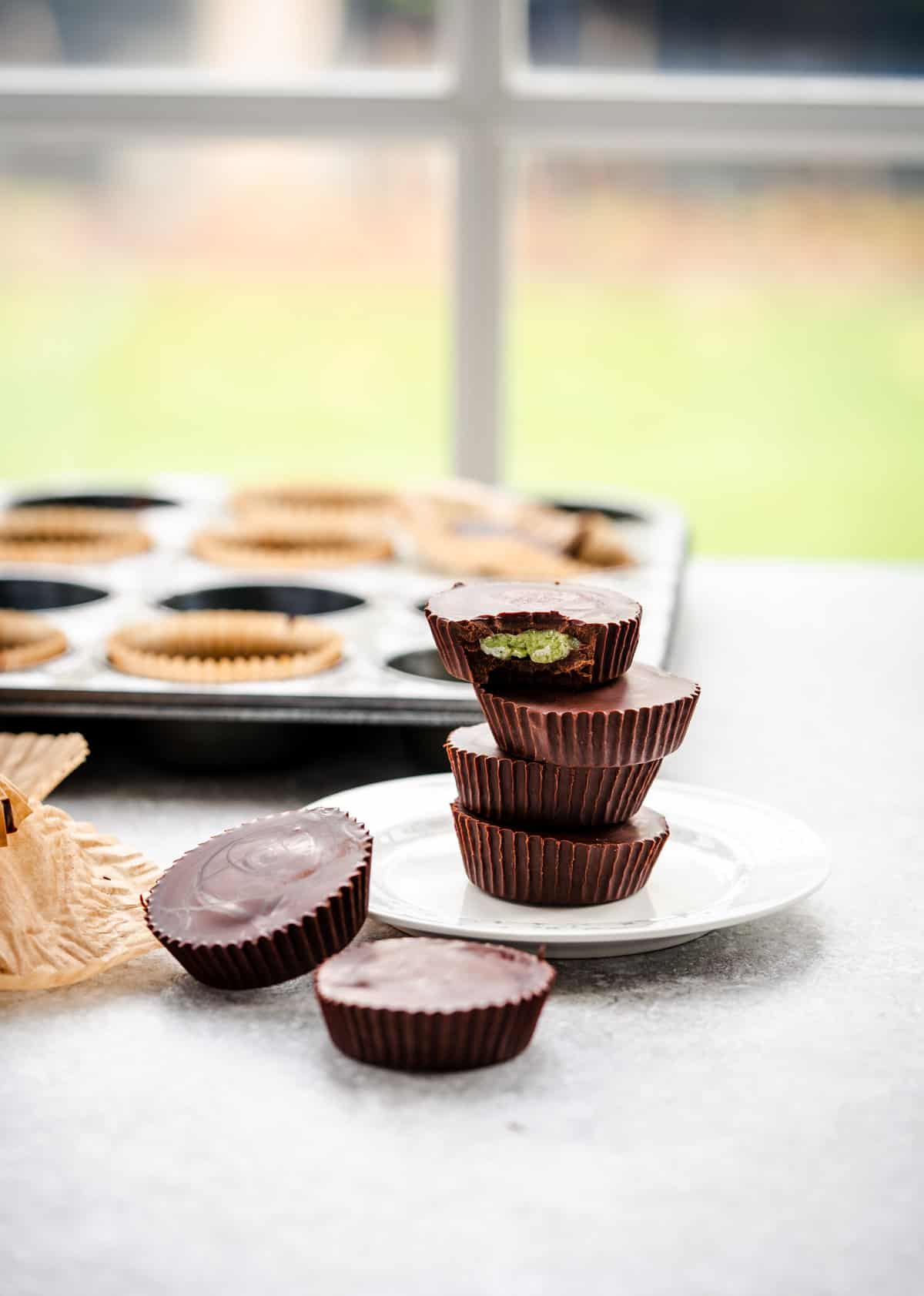 matcha dark chocolate mint cups stacked on a plate, bite out of the top one, muffin tray in background with empty wrappers to the side