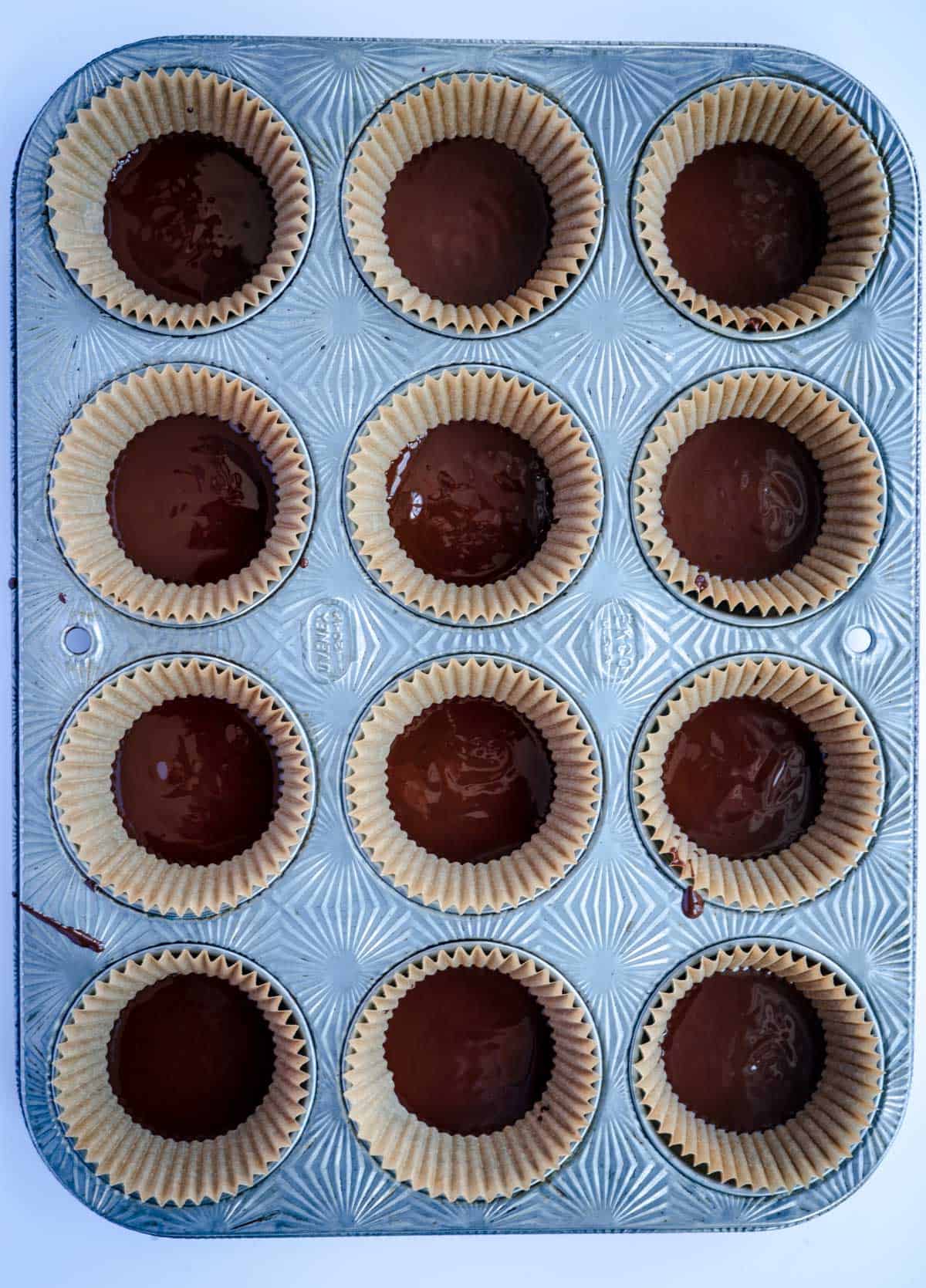 lined 12-cup muffin tin with melted dark chocolate in each cup
