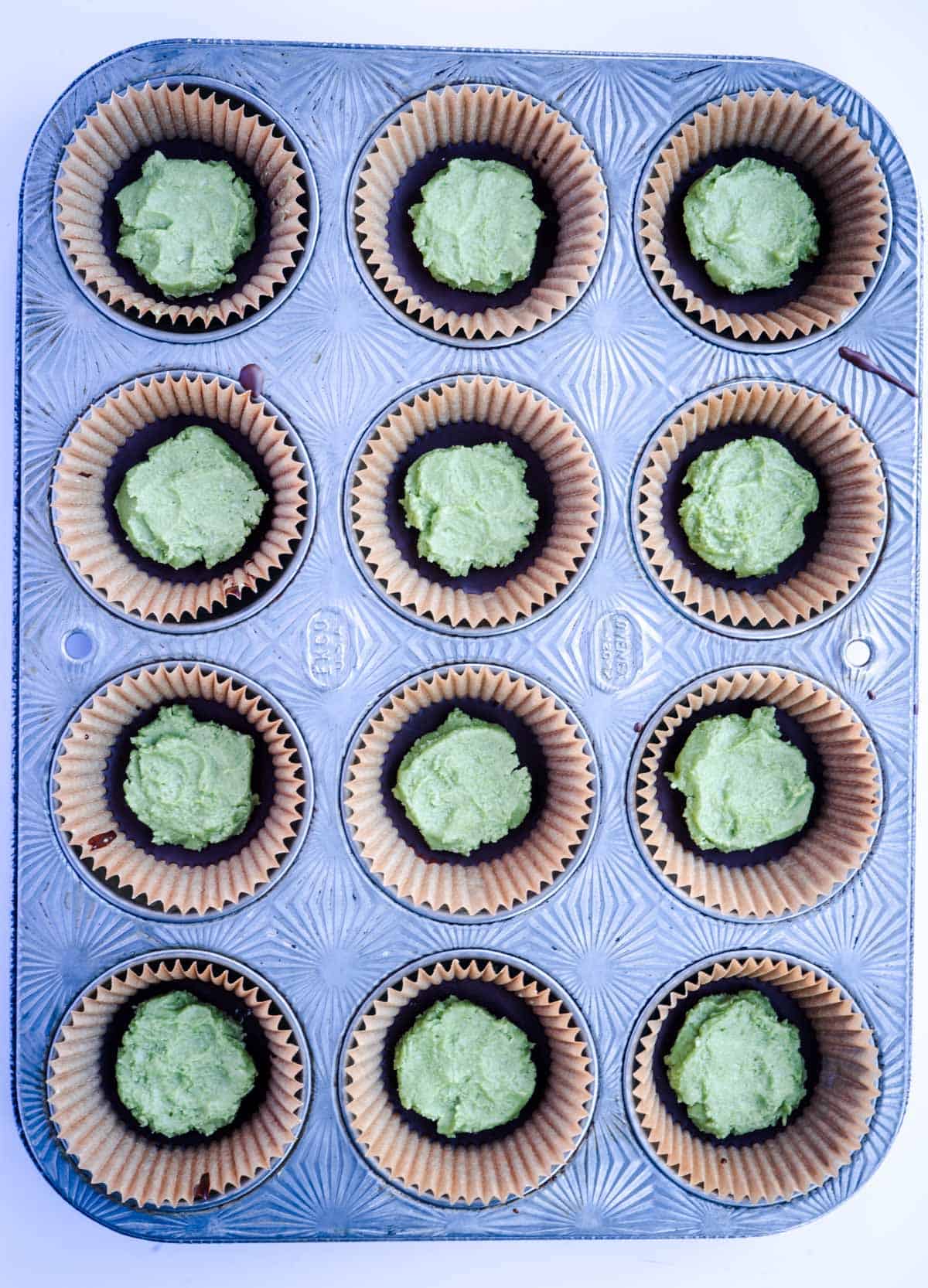 lined 12-cup muffin tin with chocolate and coconut matcha peppermint mix on top