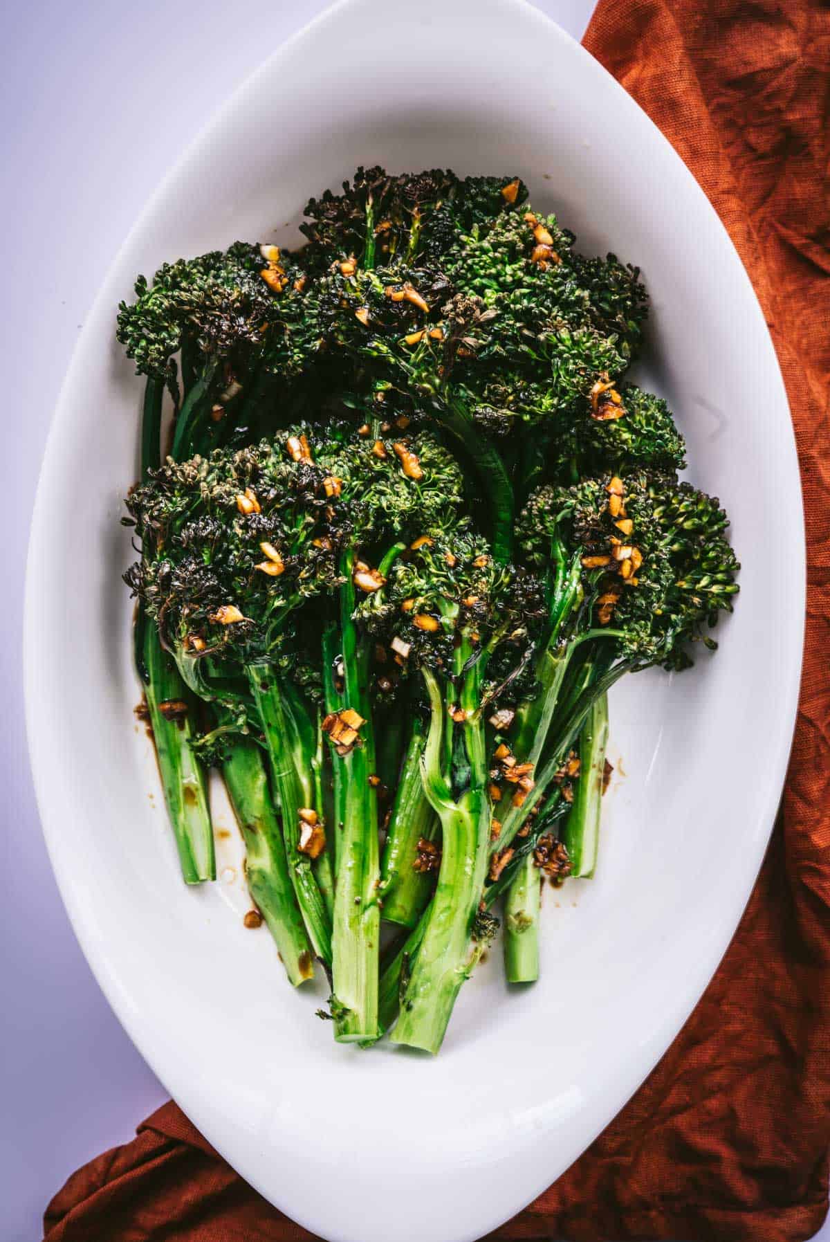 roasted broccolini on a serve dish topped with garlic, ginger, soy dressing.