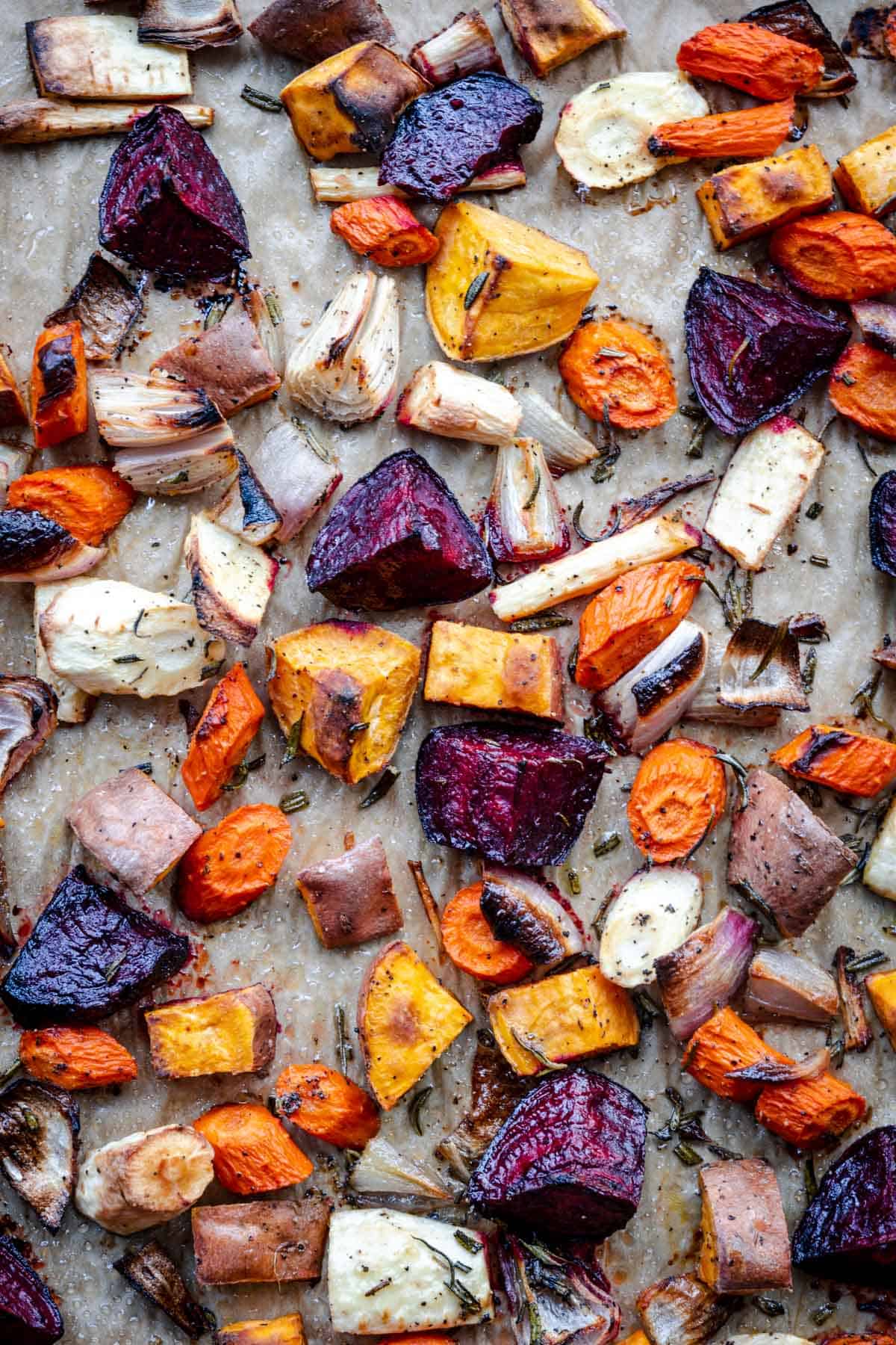 roasted assorted root vegetables on a baking tray with rosemary
