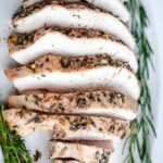 sliced roasted turkey breast on platter with herbs on the side.