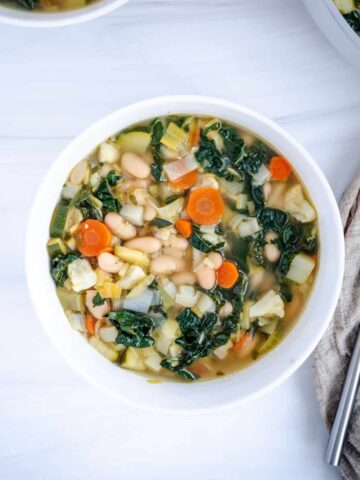 simmered white bean vegetable soup with kale in a grey pot.