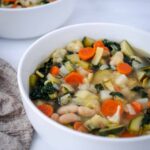 white bean vegetable soup in white bowl with beige napkin