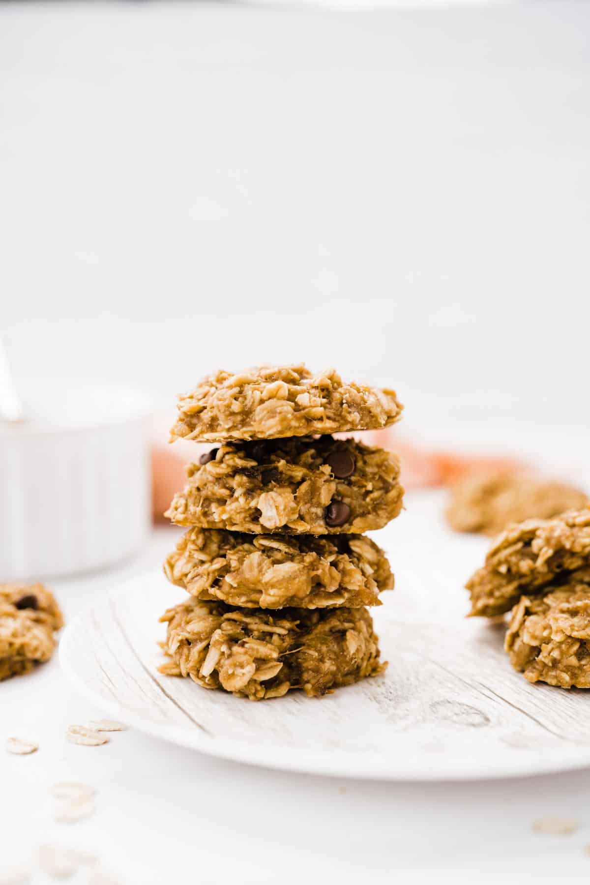 3-ingredient banana oatmeal breakfast cookies stacked on a plate with a dish of peanut butter in the background
