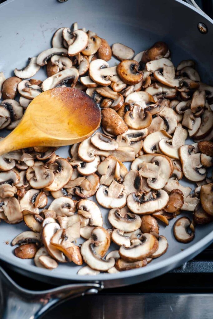 creamy mushroom in sautéing in a grey pan with wooden spoon