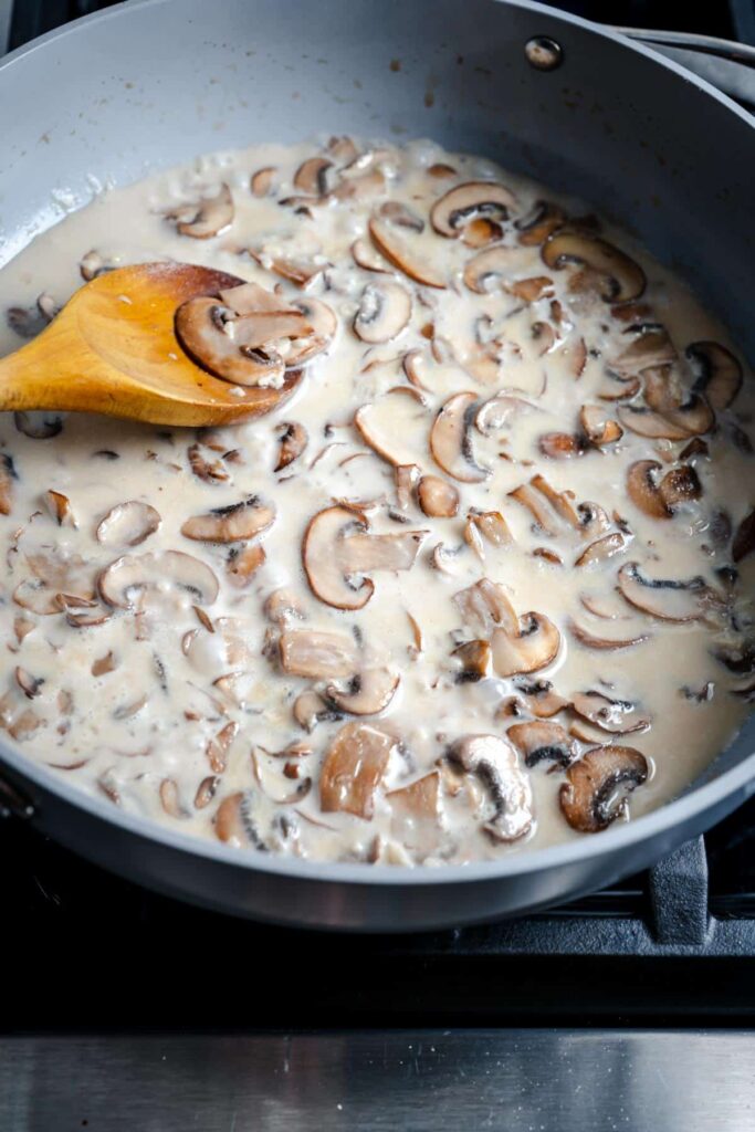 creamy mushroom sauce with coconut milk in grey pan with wooden spoon