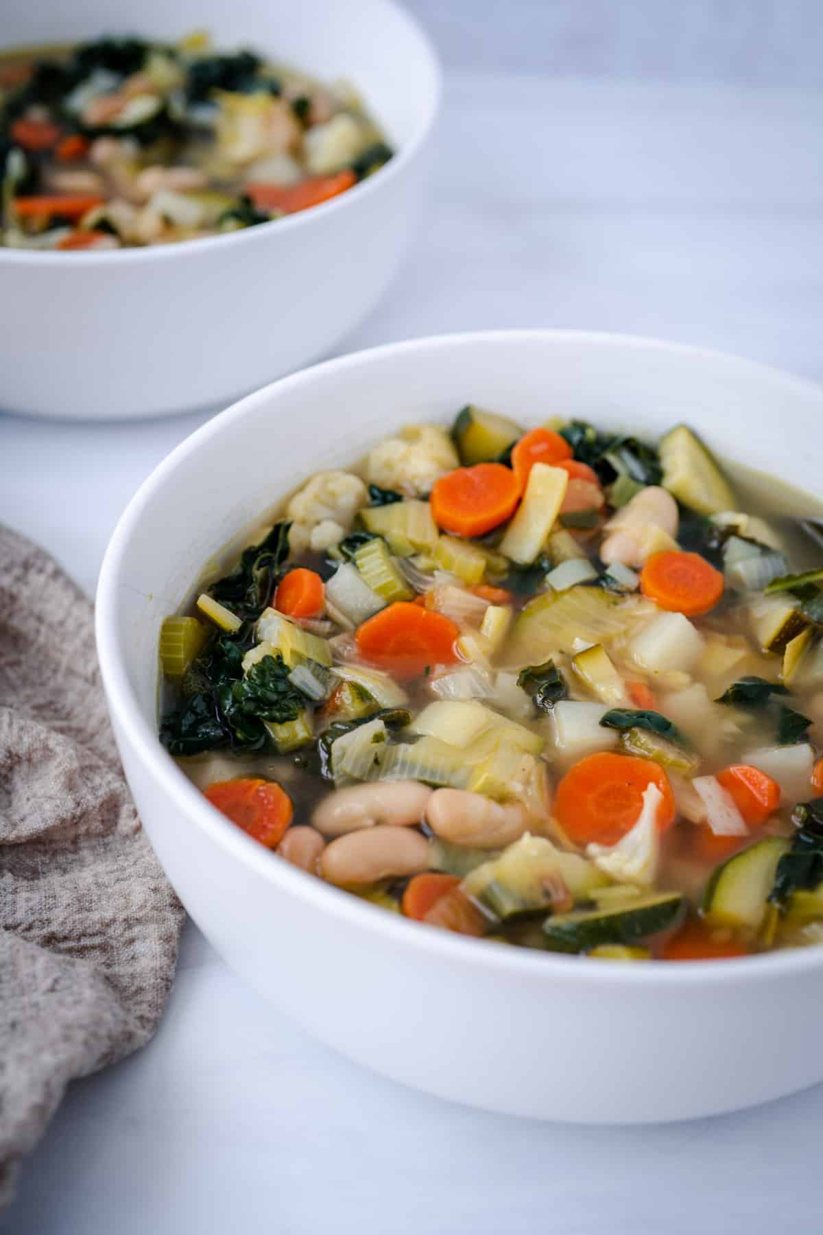 white bean vegetable soup with kale in white bowl with beige napkin