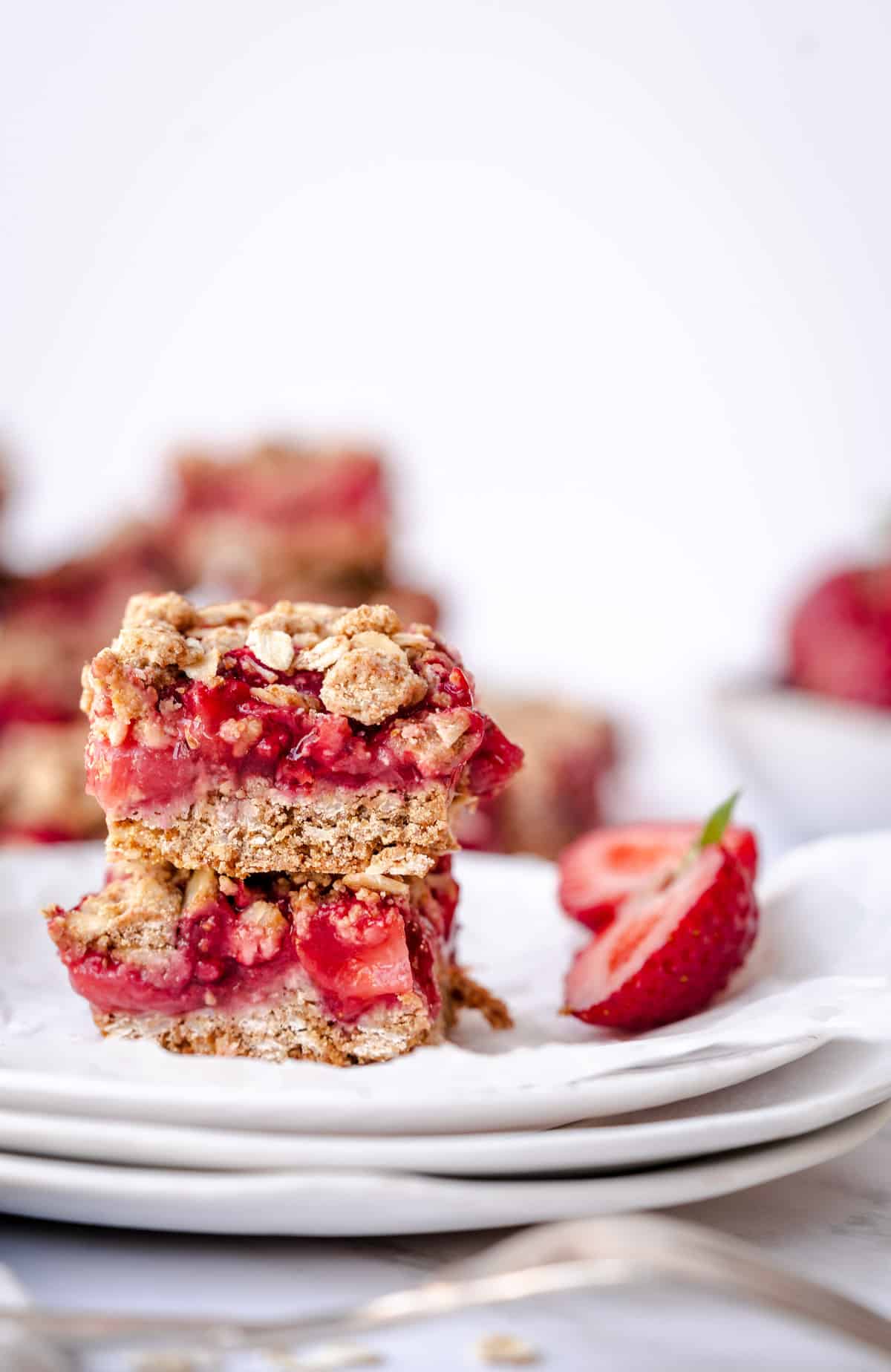 two strawberry crumble bars on white plate with cut strawberry.