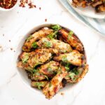 zesty baked italian style chicken wings on white plate with sprinkle of hot pepper flakes.