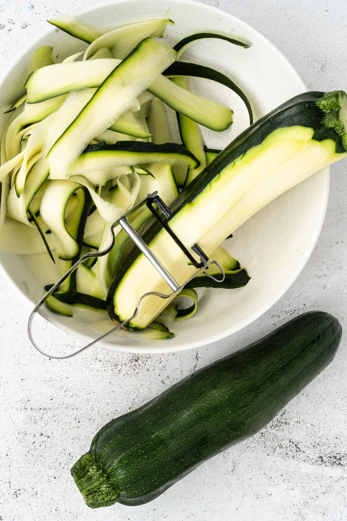 process shot of making zucchini ribbons with vegetable peeler.
