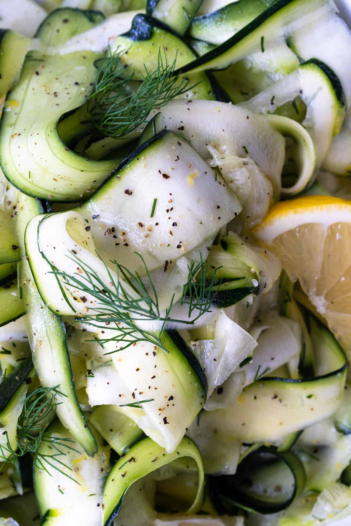 up close image of shaved zucchini ribbons with lemon, zest, dill, salt and pepper.
