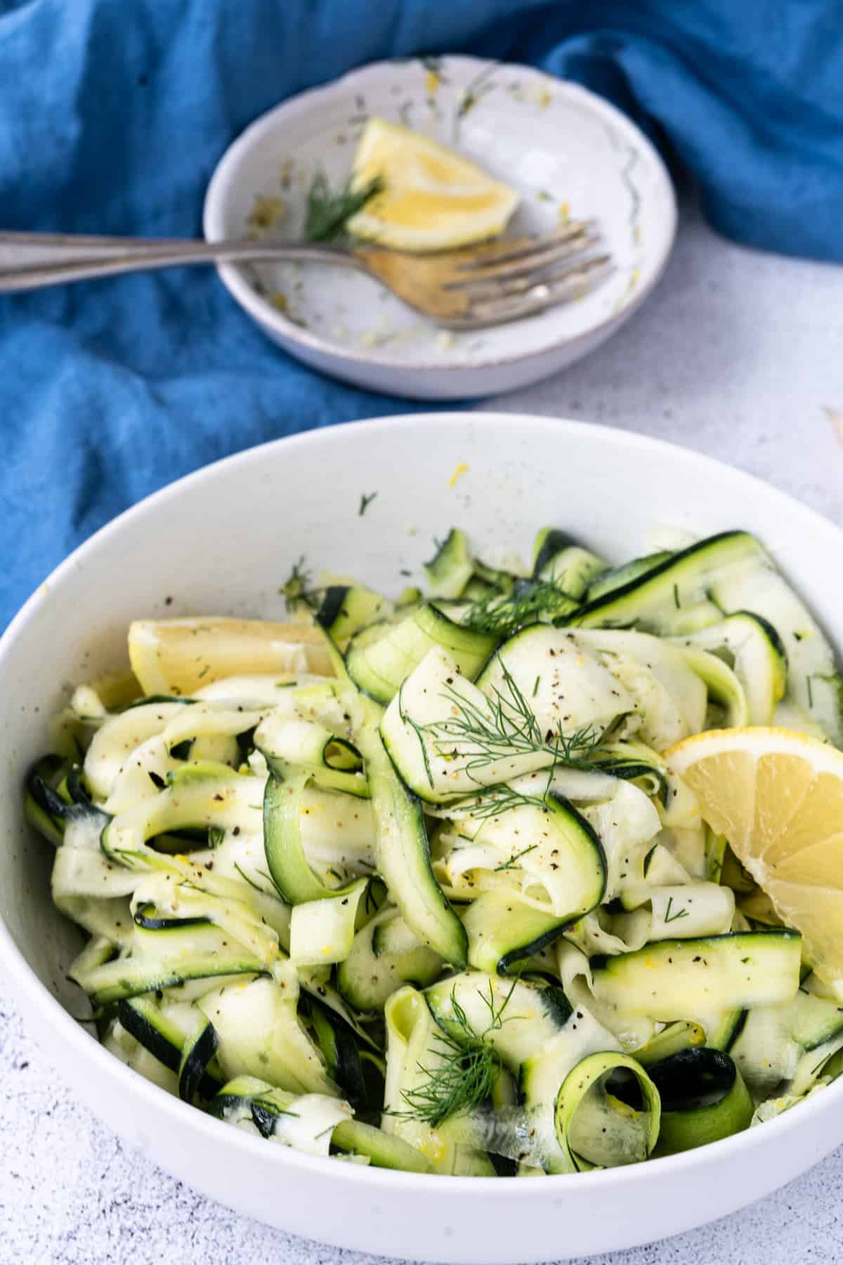 shaved zucchini ribbon salad with lemon and dill on white dish with lemon slice.