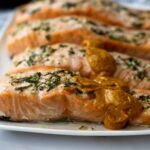 up close of baked lemon garlic salmon filets with herbs on top and a dollop of romesco sauce.
