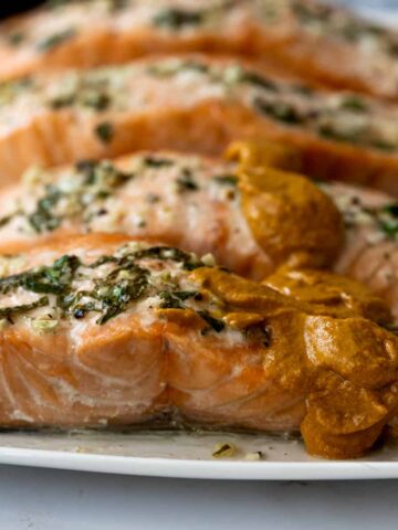 up close of baked lemon garlic salmon filets with herbs on top and a dollop of romesco sauce.