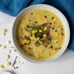 spicy creamy potoato corn chowder in white bowl with red chili flakes and chives topping..