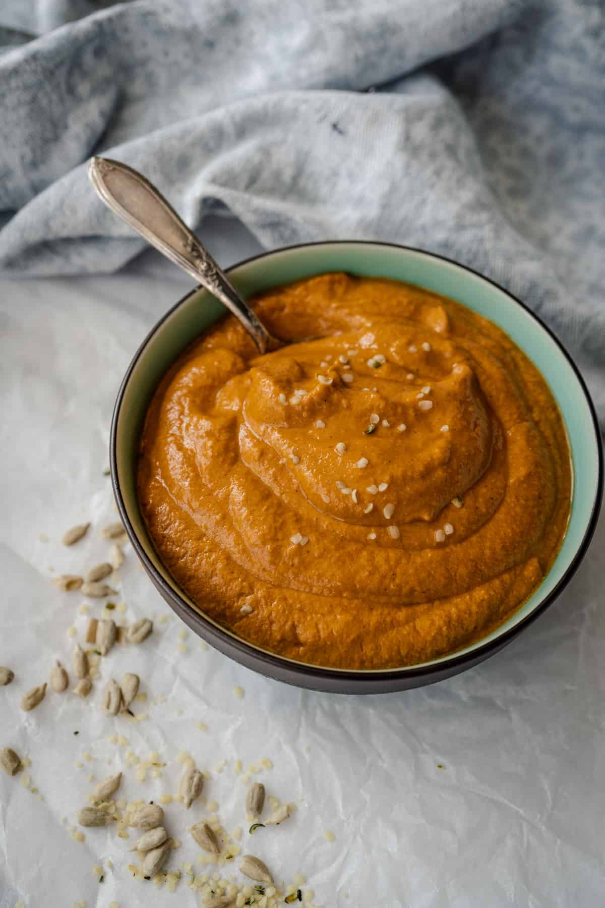 nut free romesco sauce in bowl with serve spoon and sunflower seeds scattered.