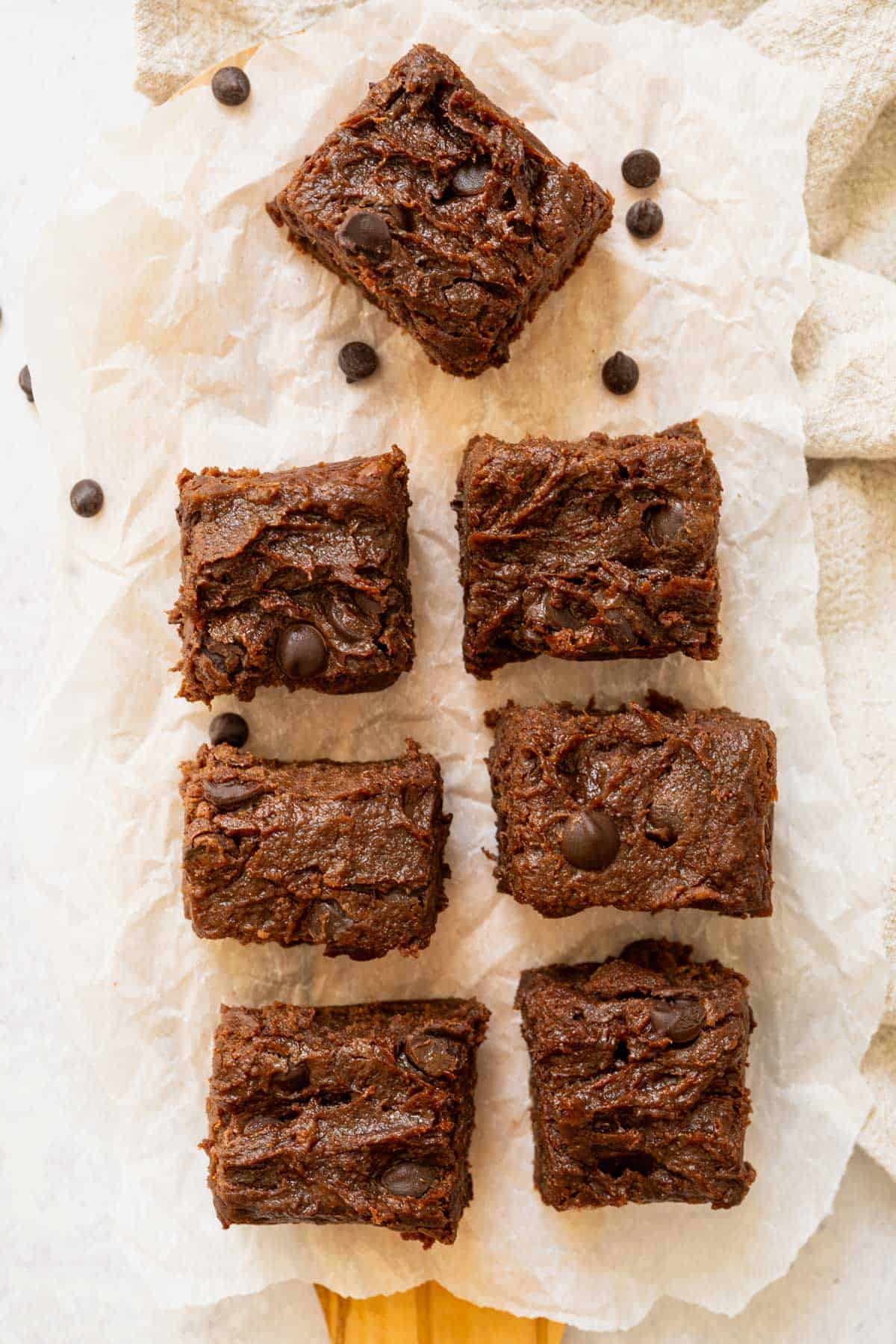 7 cut brownies on parchment paper with scattering of chocolate chips.