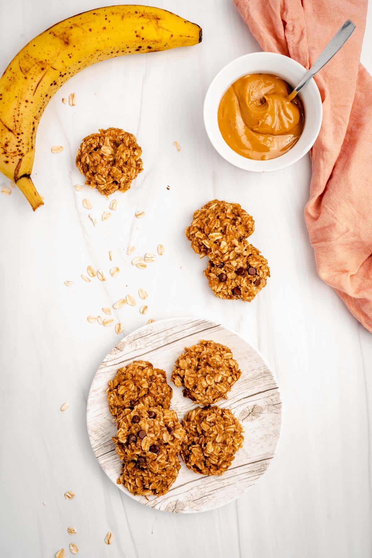cookies on plate with 3 on counter plus a ripe banana and bowl of peanut butter with spoon.