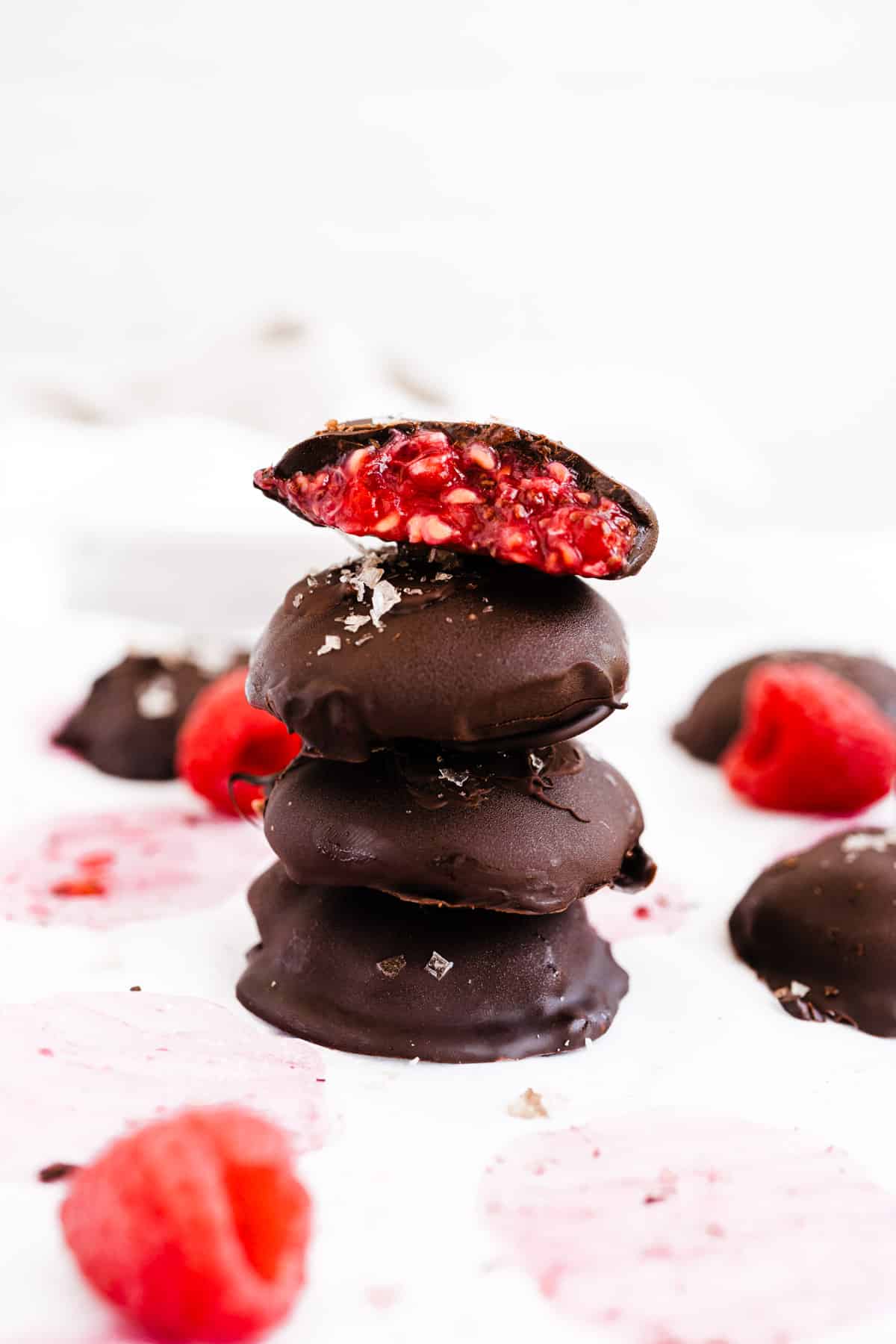 Chocolate covered raspberry chia bites stacked four high with the top one cut in half to reveal filling.