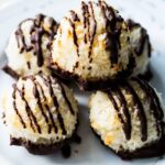Five peppermint coconut macaroons drizzled in dark chocolate stacked together on a white plate.