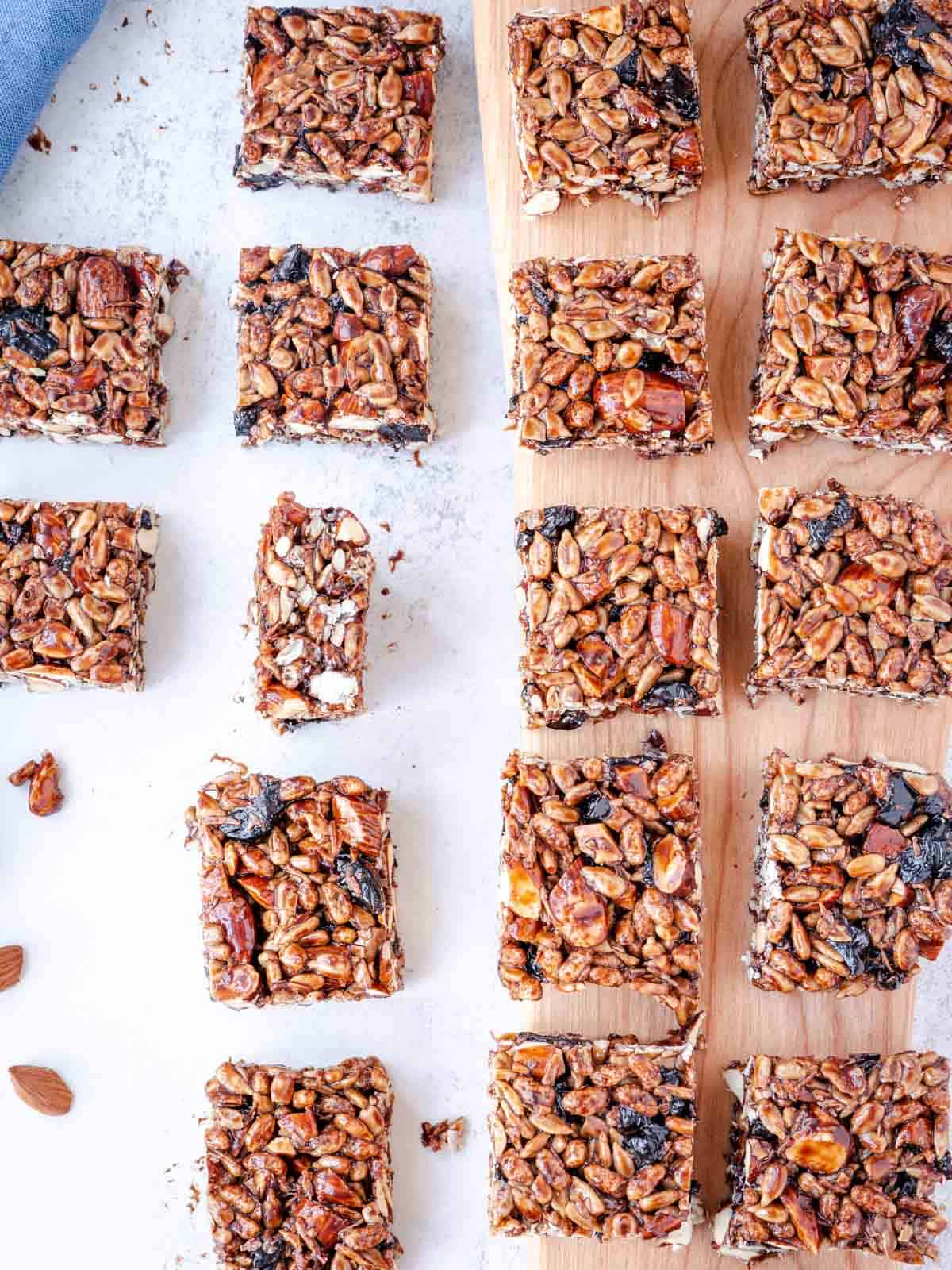 Almond cherry pepita bars cut into squares on a wood board with a blue napkin.