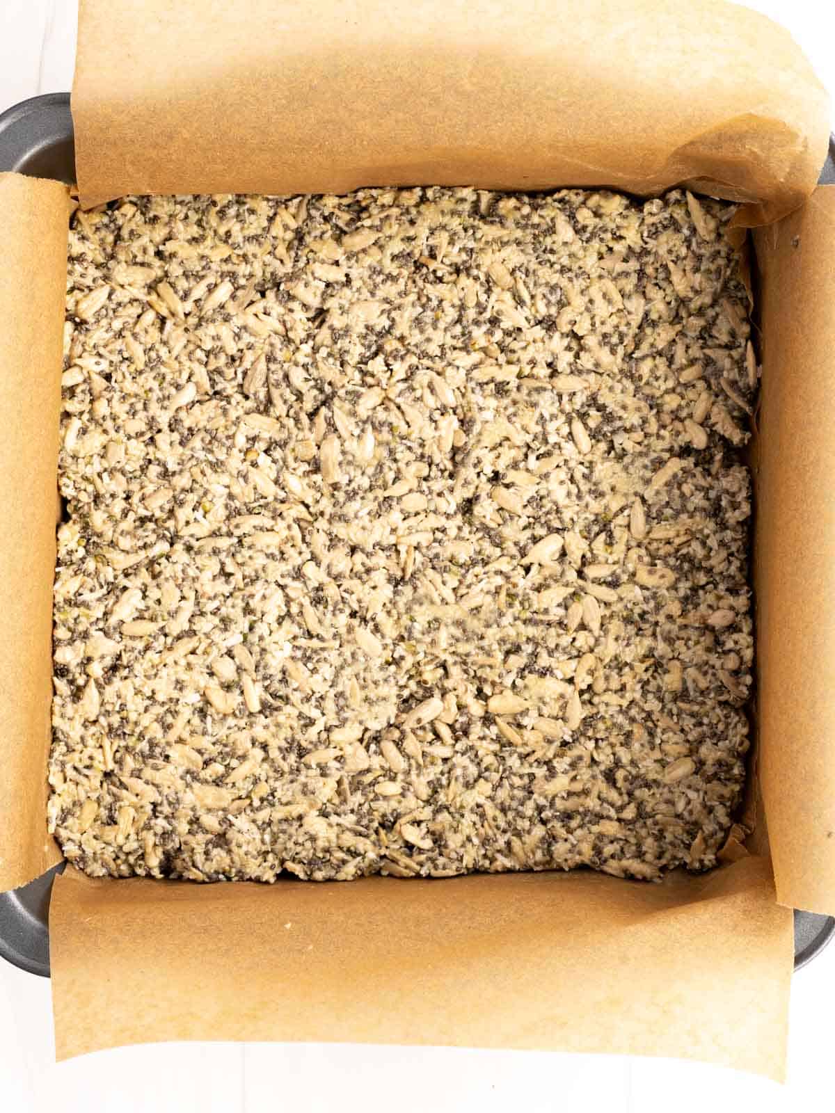 Energy snack and seed bar ingredients pressed into an 8x8-inch parchment lined pan.