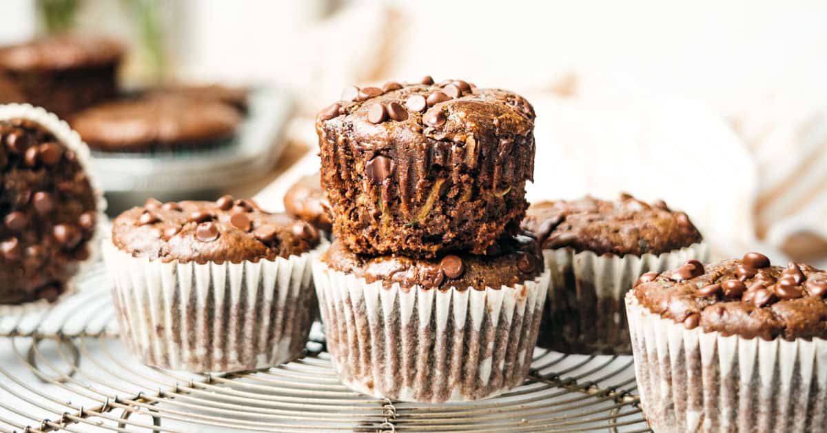 Two double chocolate zucchini muffins stacked with extra muffins around.