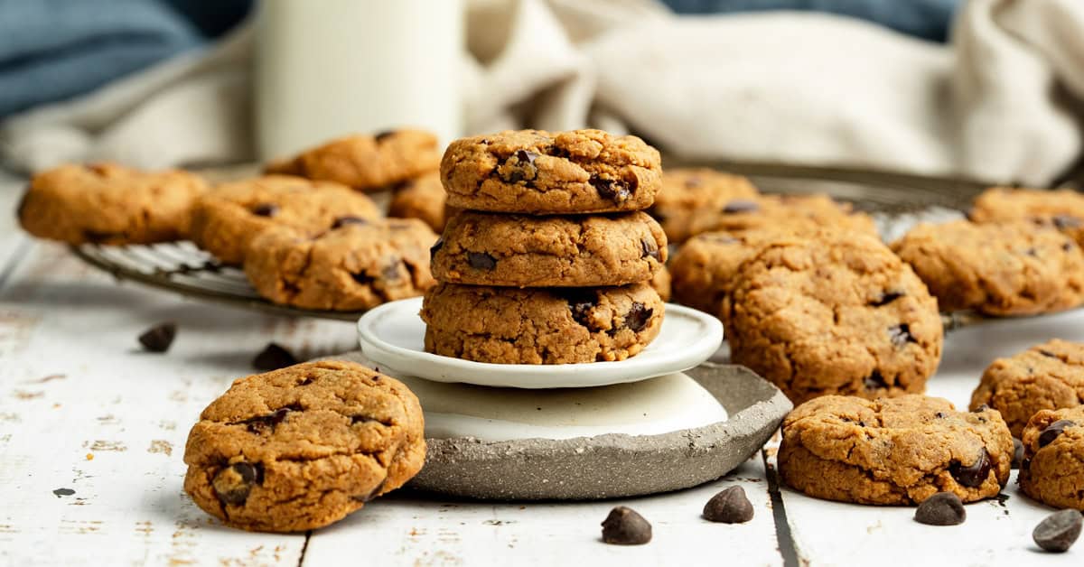 Three vegan peanut butter chocolate chip cookies stacked on a white dish with cookies around.