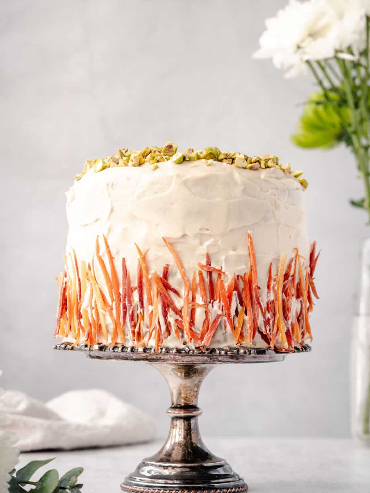 Gluten free carrot cake decorated on cake stand with daisies in background.