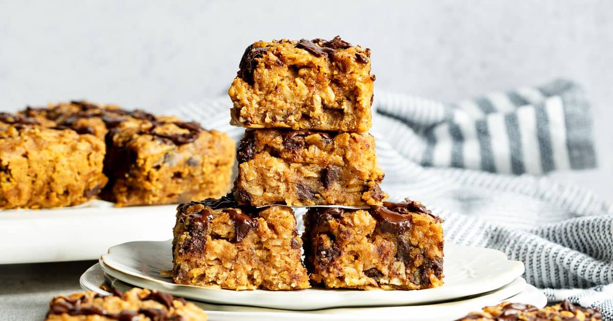 Four sweet potato oat bars stacked on a white plate with blue striped napkin.