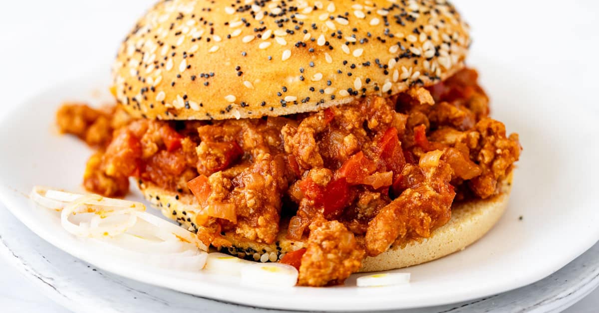Gluten free chicken sloppy joes in gluten free seeded bun on white plate.
