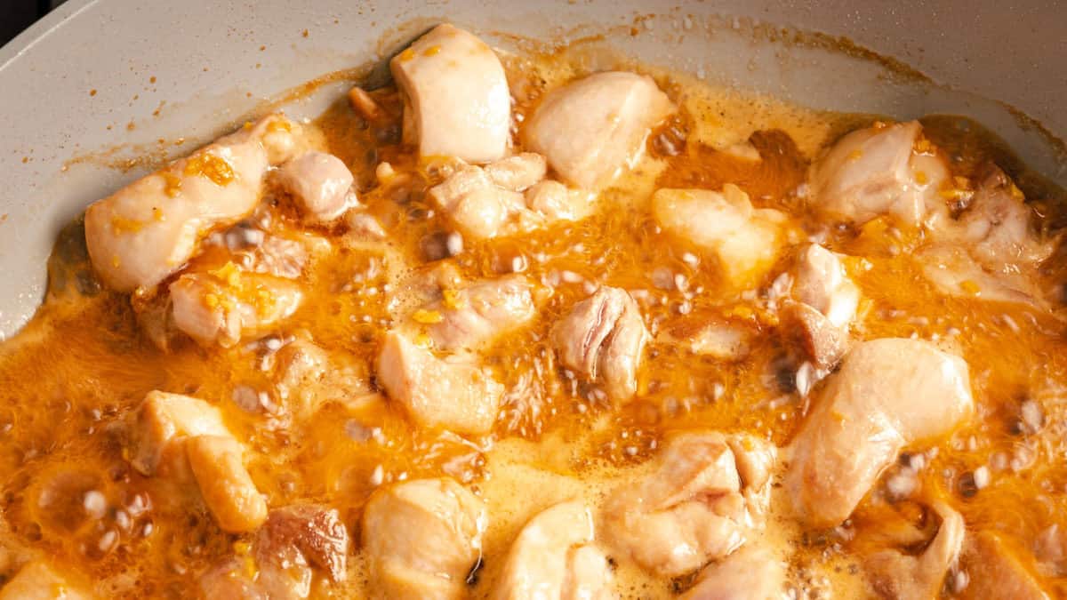 Teriyaki chicken sautéing in a grey pan.