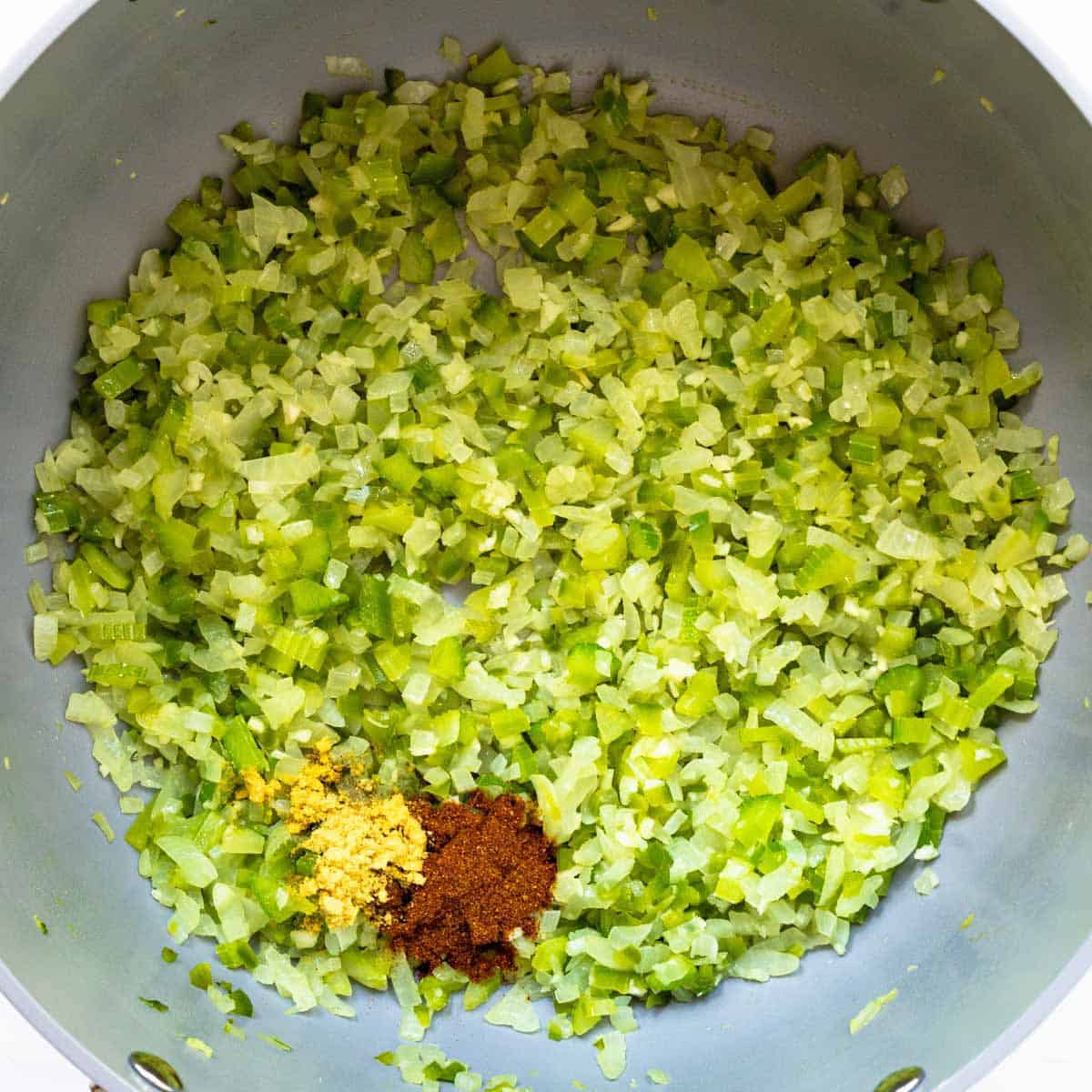 Sauteed celery, garlic and onions with added spices in grey soup pot.