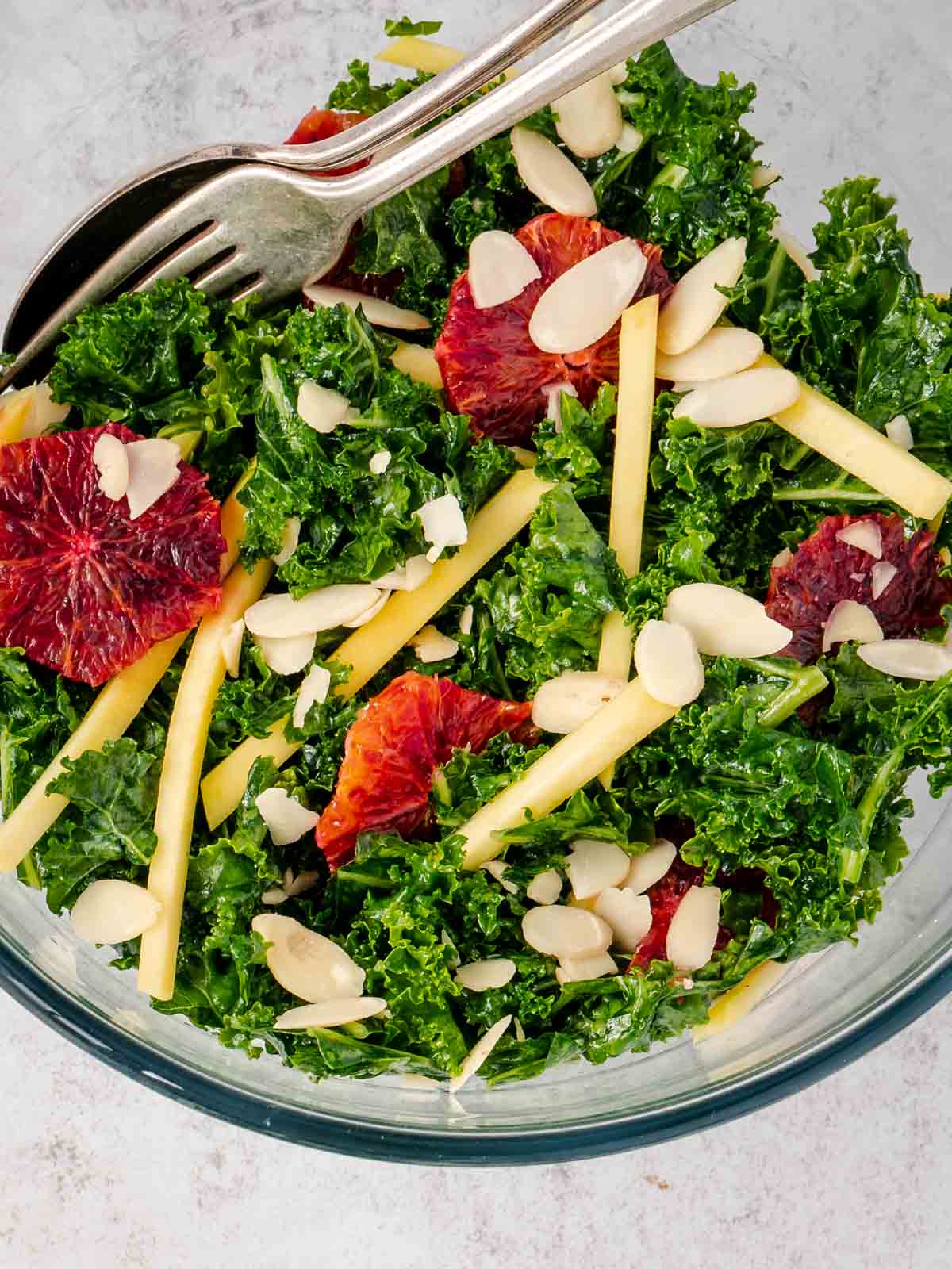Kale mango salad recipe in a clear bowl with a fork and spoon.