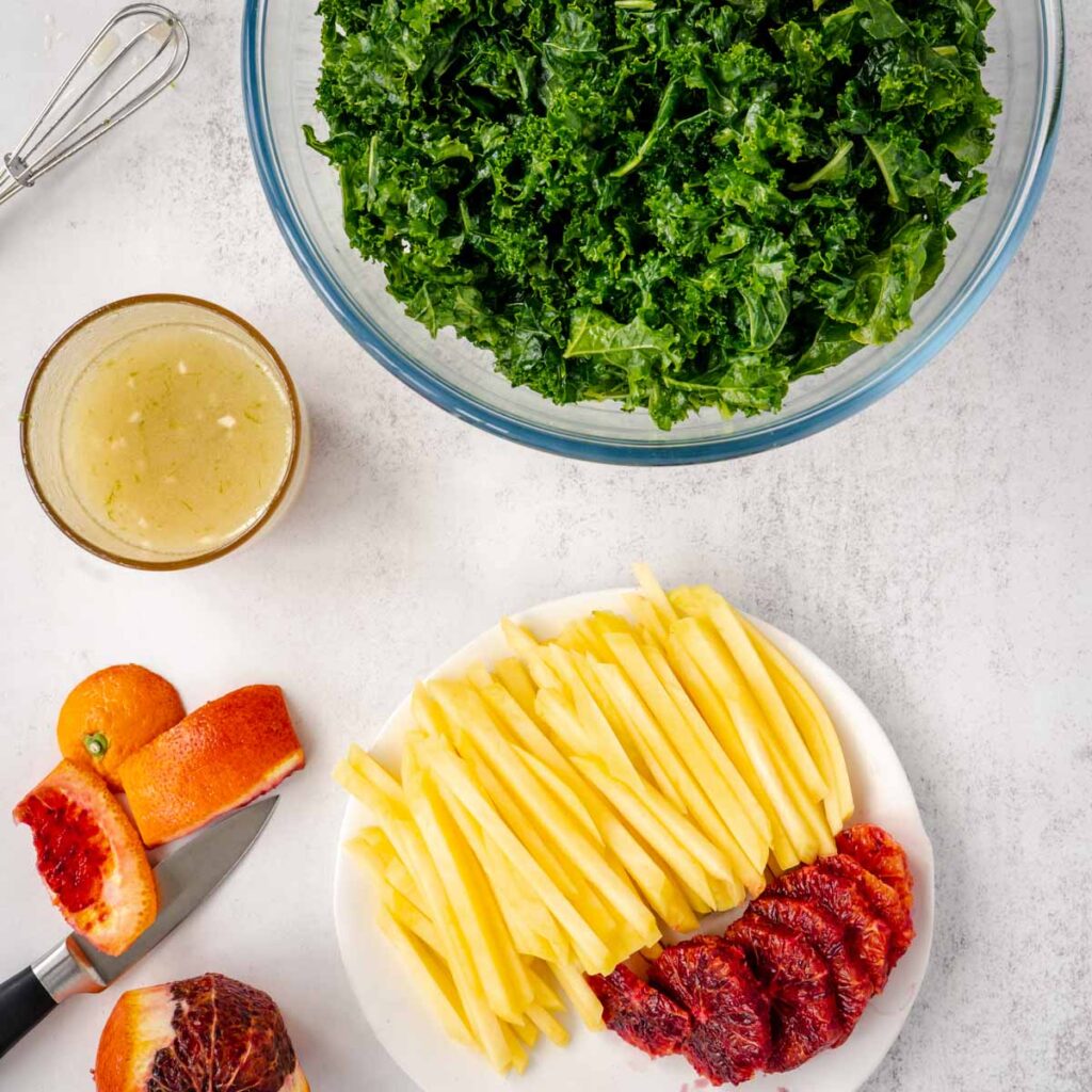 Ingredients for kale mango salad ready to be combined into a salad in a clear bowl.