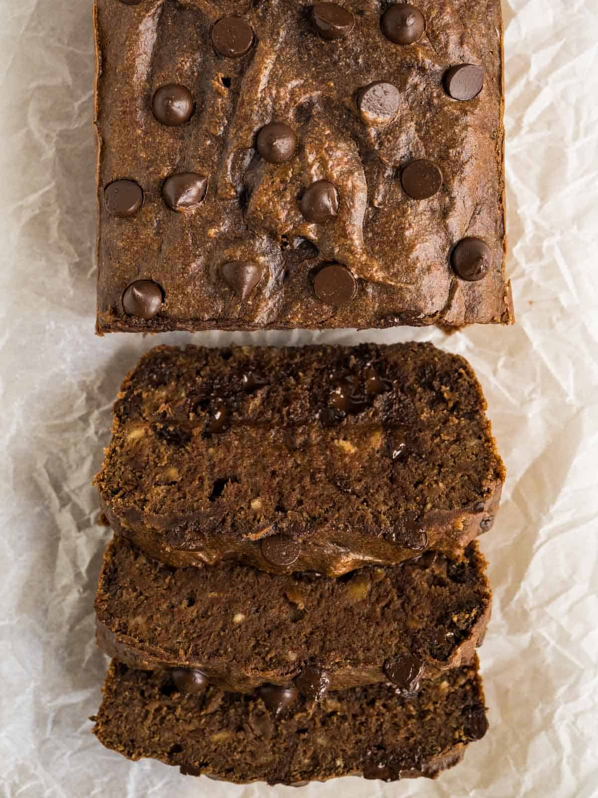 Baked chocolate bread partially sliced on parchment paper.